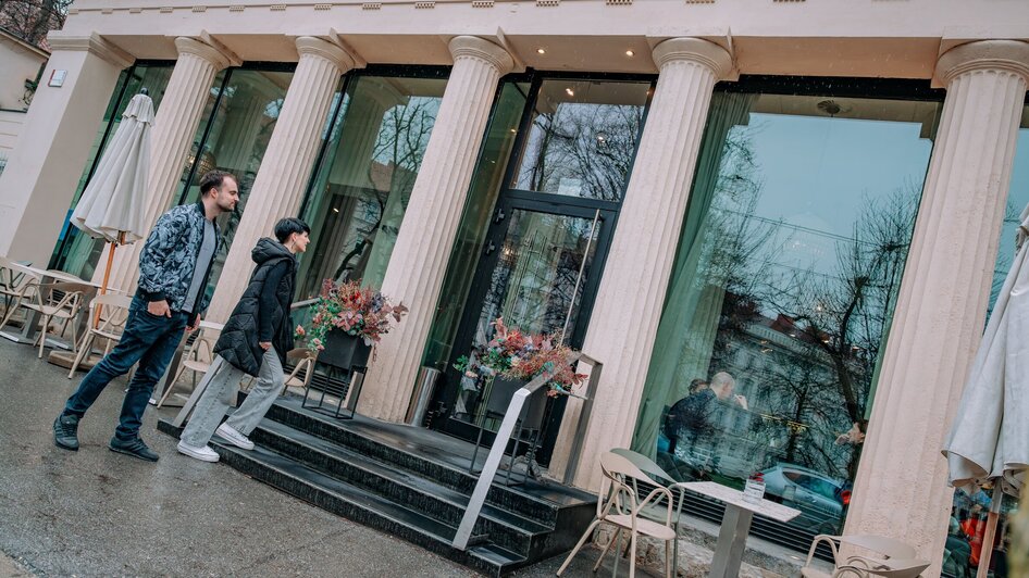 Zwei Personen gehen am Café Promenade in Graz vorbei.