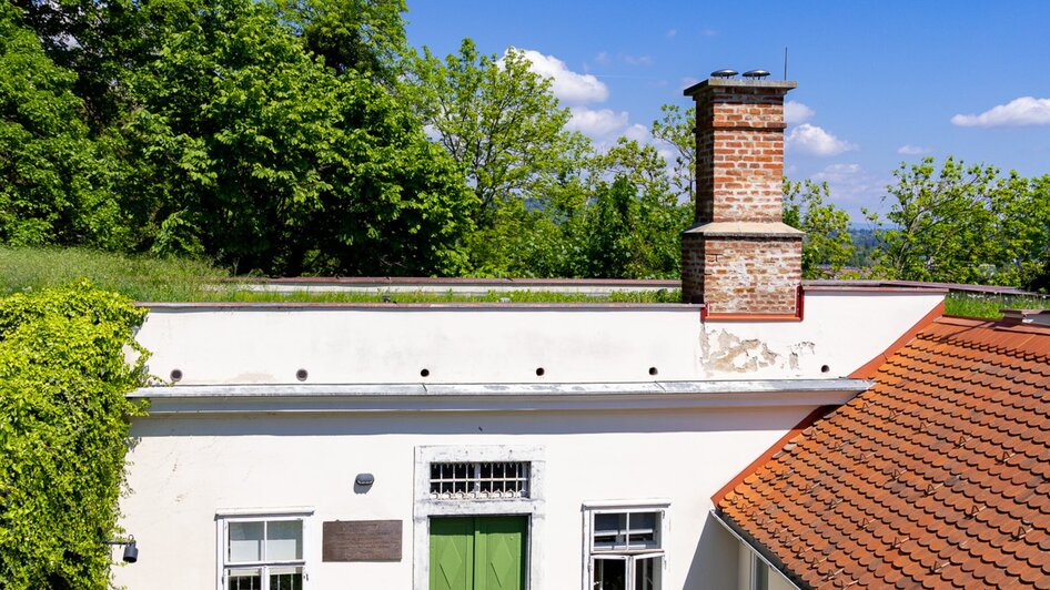 Das Cerrini-Schlössl mit grünem Eingang und Kamin, umgeben von Bäumen und blauem Himmel. | © Graz Tourismus - Harry Schiffer