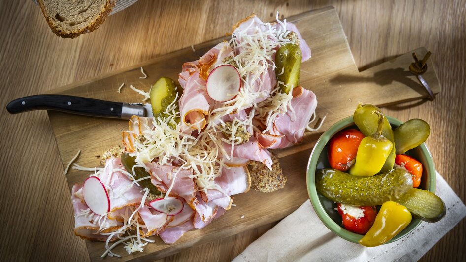 Ein Holzbrett mit Aufschnitt, Käse, Gurken und einem bunten Antipasti-Schälchen. | © Kaiser Greissler - Werner Krug