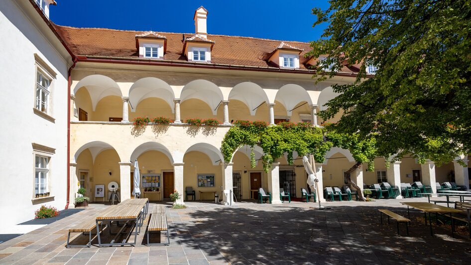 Innenhof mit Arkaden und Bäumen, strahlend blauer Himmel.