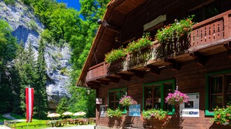 Ein Holzhaus mit Blumen über dem Eingang, umgeben von Bäumen und Felsen. | © TV Region Graz - Harry Schiffer