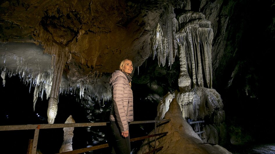 Frau steht in der Lurgrotte Semriach und bewundert beeindruckende Stalaktiten. | © Region Graz - Tom Lamm