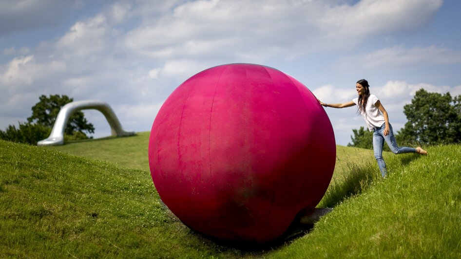 Eine Frau mit einer großen pinken Kugel im Österreichischen Skulpturenpark. | © Region Graz - Tom Lamm