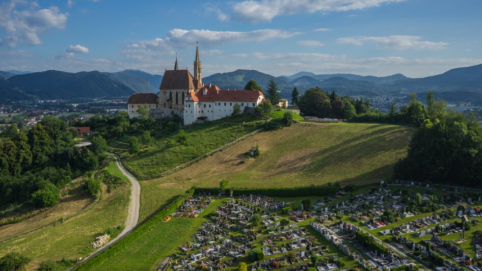 Luftaufnahme der Wallfahrtskirche Maria Strassengel mit einem Friedhof im Vordergrund.